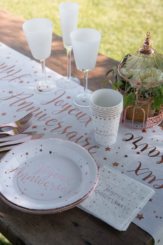 Mise en situation sur une table des serviettes en papier Joyeux Anniversaire pour fête rose gold à motifs étoiles roses