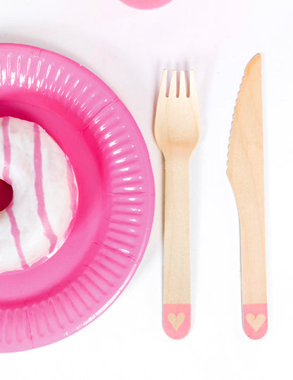 Gros plan sur la fourchette et le couteau des couverts en bois jetables avec cœur pour fête rose