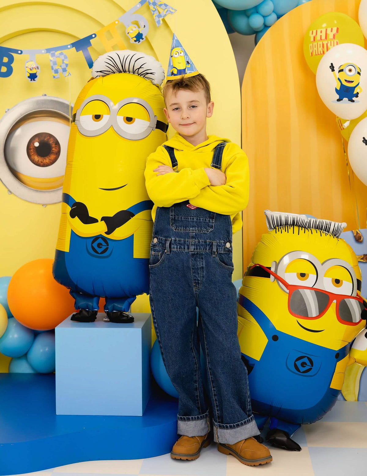 Enfant debout à côté du ballon aluminium Tim Minions™