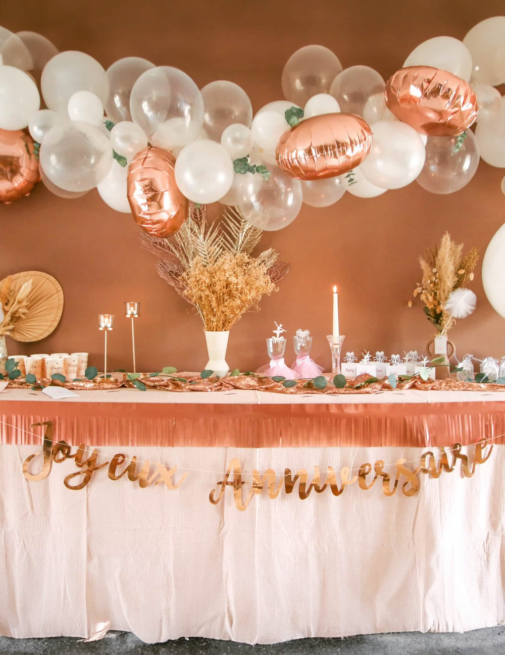 Mise en situation sur une table d'anniversaire du kit arche de 70 ballons rose gold avec eucalyptus et roses