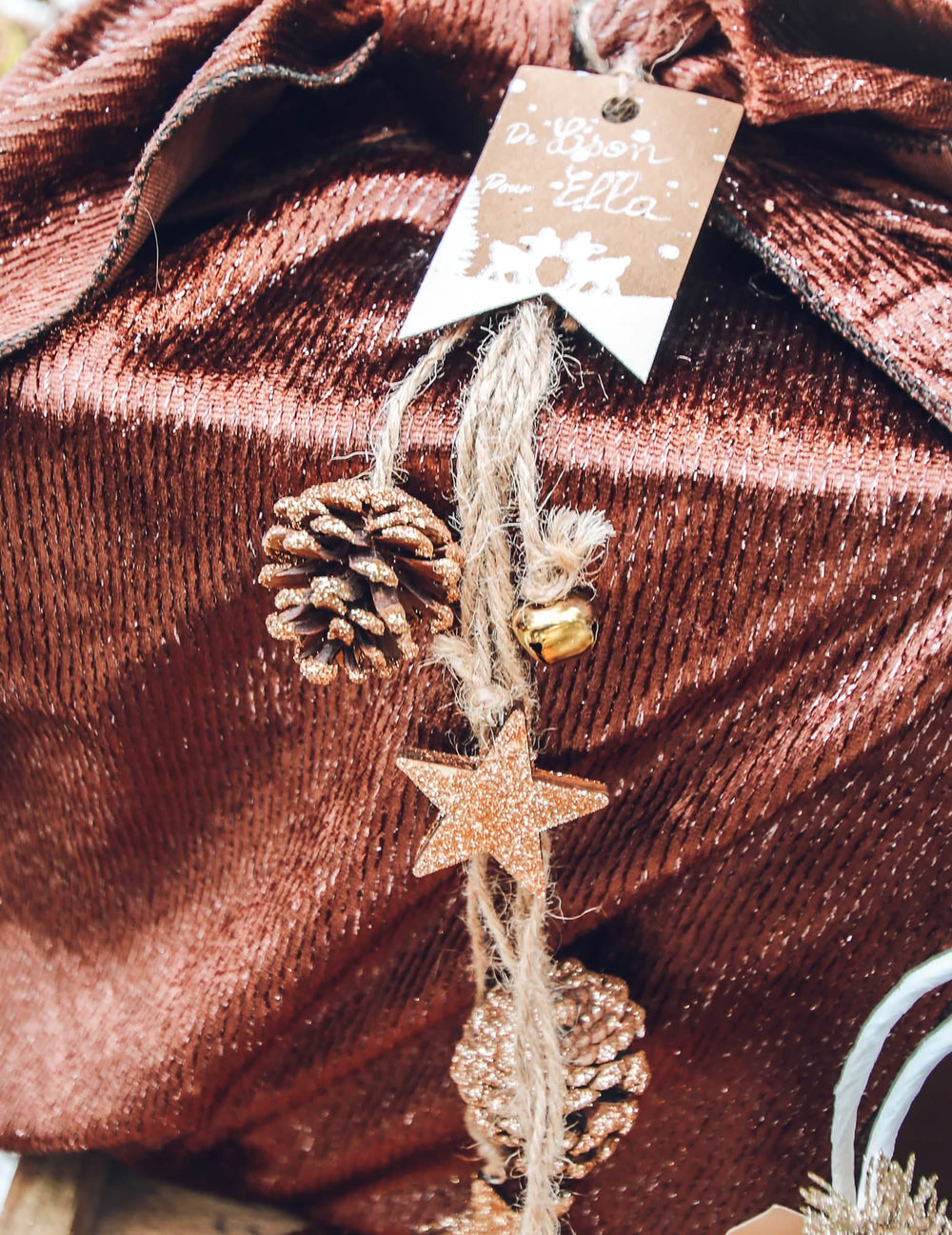 Mise en situation sur un paquet cadeau de la suspension pommes de pin et étoiles bois pour décoration paillettes cuivre